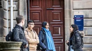 A group of four students stand outside a building talking