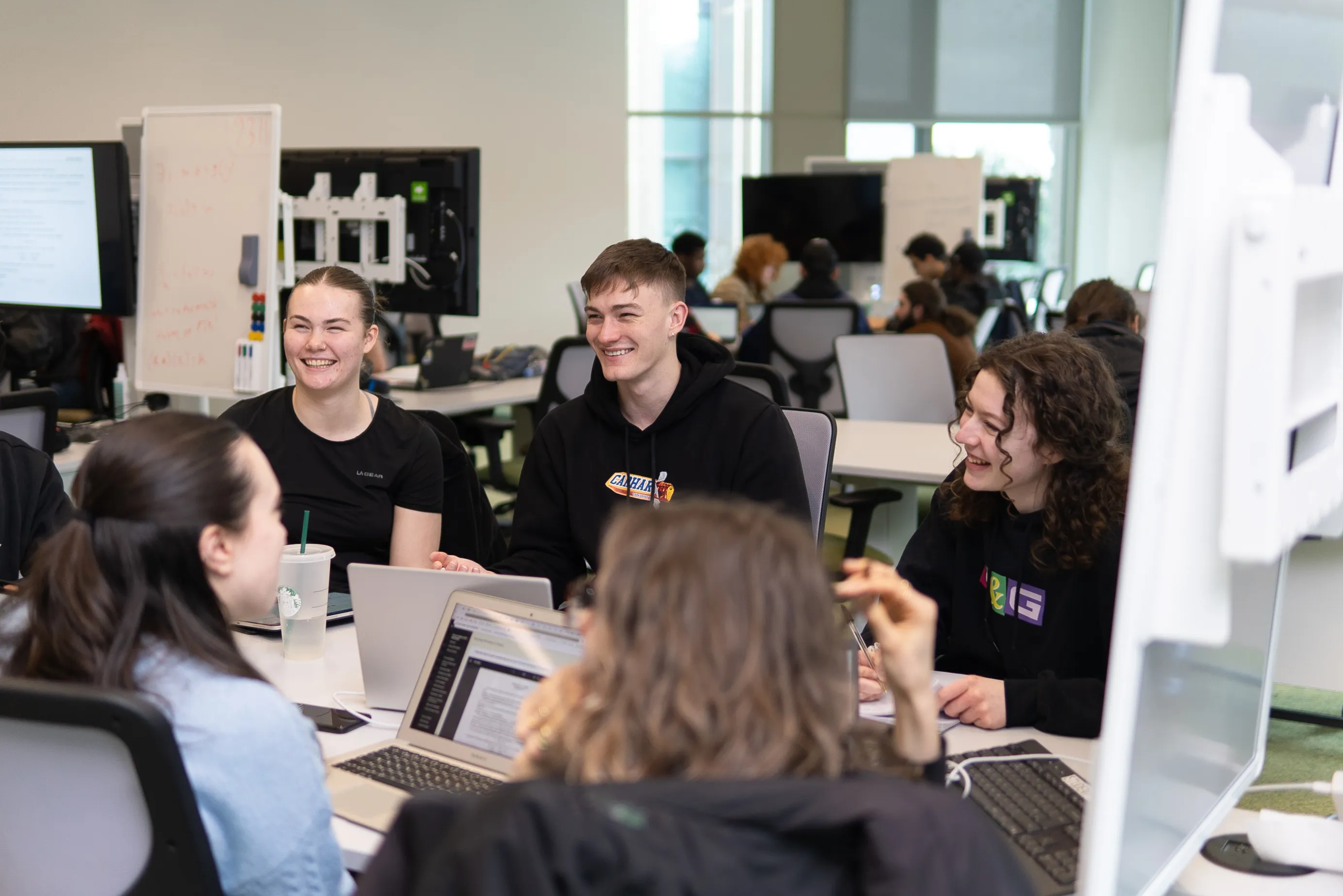 A group of students gather around a table working on their laptops.