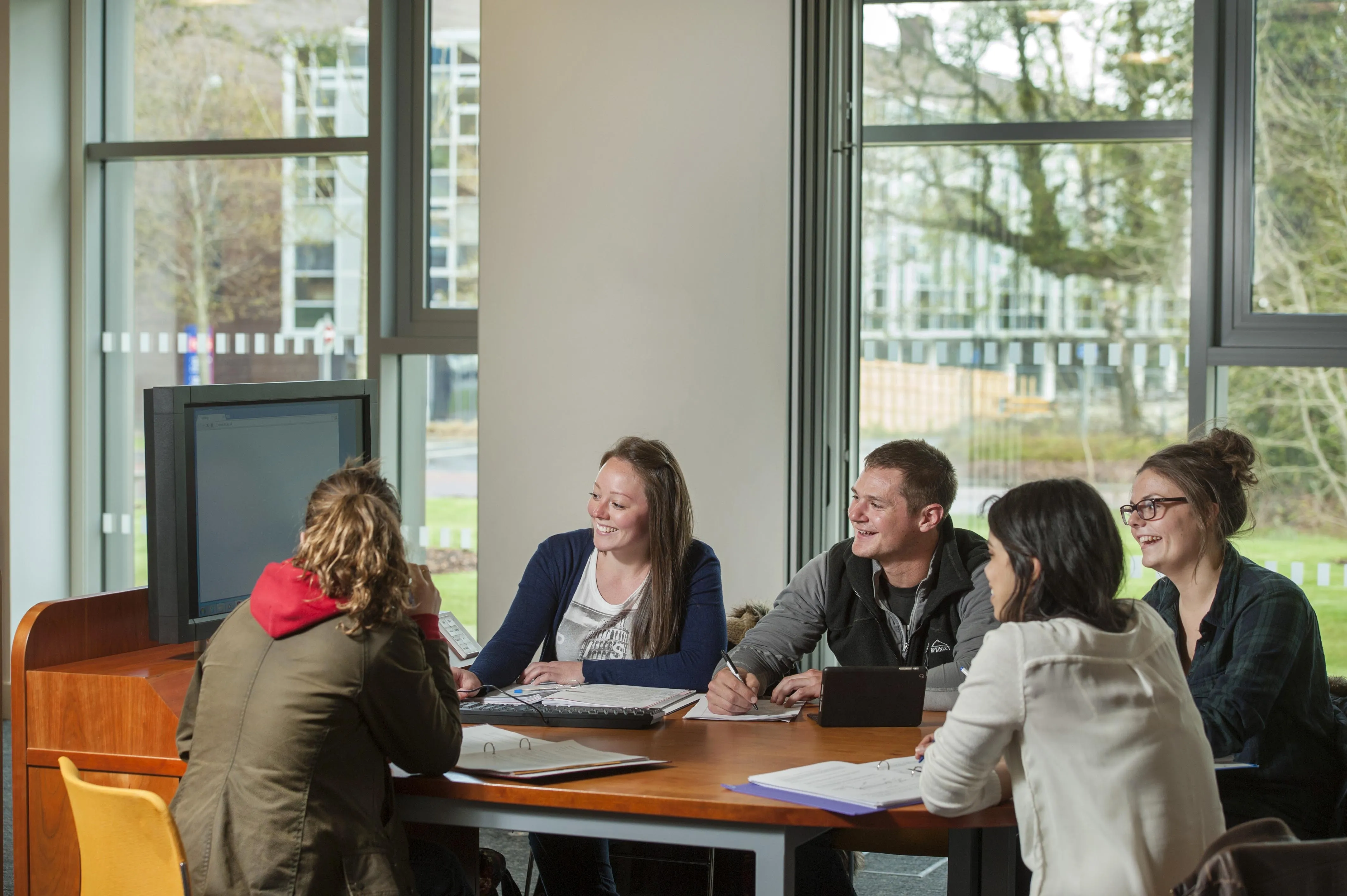 Five students sit around a table working on a large screen.